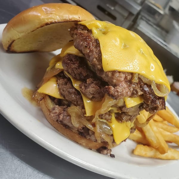 A towering triple cheeseburger with melted cheese and caramelized onions, served with fries.