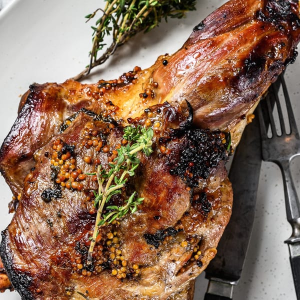 Close-up of a grilled meat dish with whole grain mustard and fresh thyme sprigs.