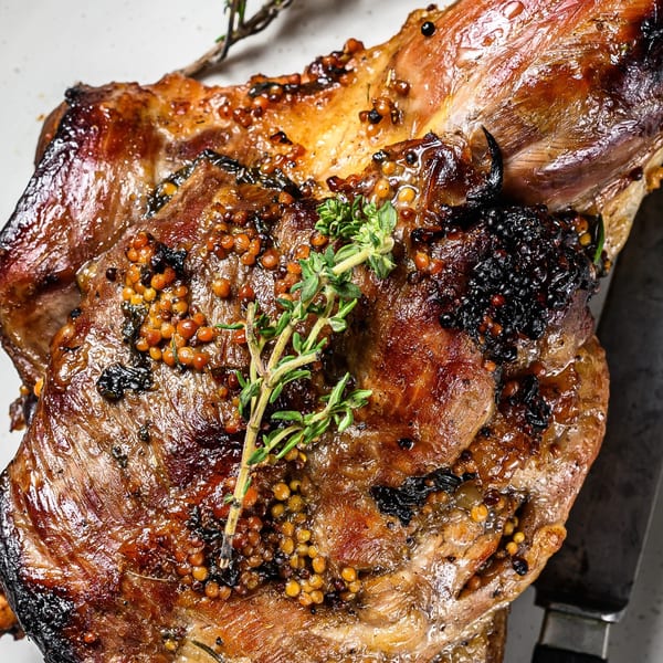 Close-up of a glazed, roasted meat dish, garnished with mustard seeds and fresh thyme.