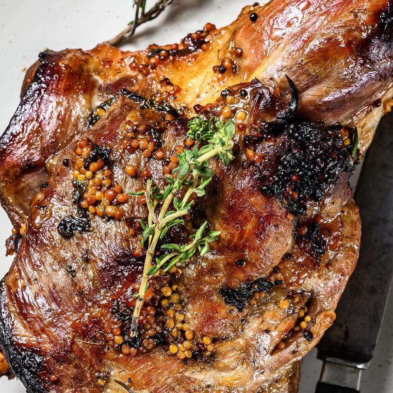 Close-up of a glazed, roasted meat dish, garnished with mustard seeds and fresh thyme.