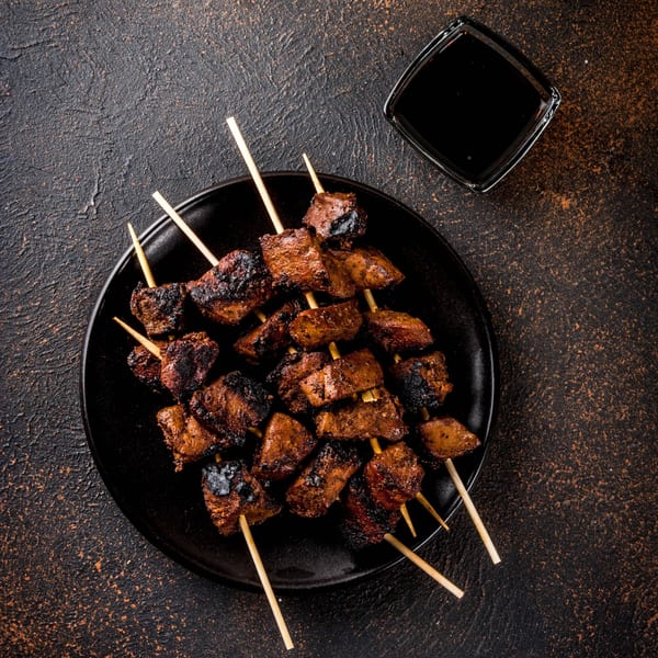 Grilled meat skewers, likely from Papas Bar, served on a black plate with a side of dark sauce.