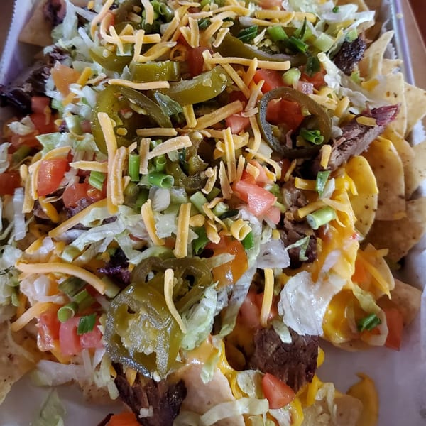 Loaded nachos from Papas Bar, topped with cheese, jalapeños, lettuce, tomatoes, and meat.